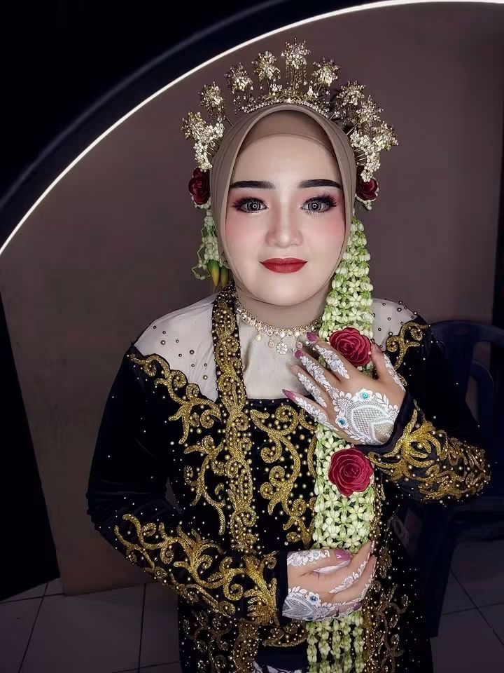 Pengantin duduk di depan cermin berlampu dengan mahkota emas dan rangkaian melati.