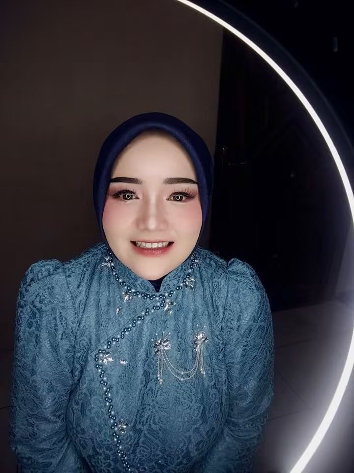 Potret riasan dengan kebaya brokat hijau kebiruan di bawah lampu cincin.
